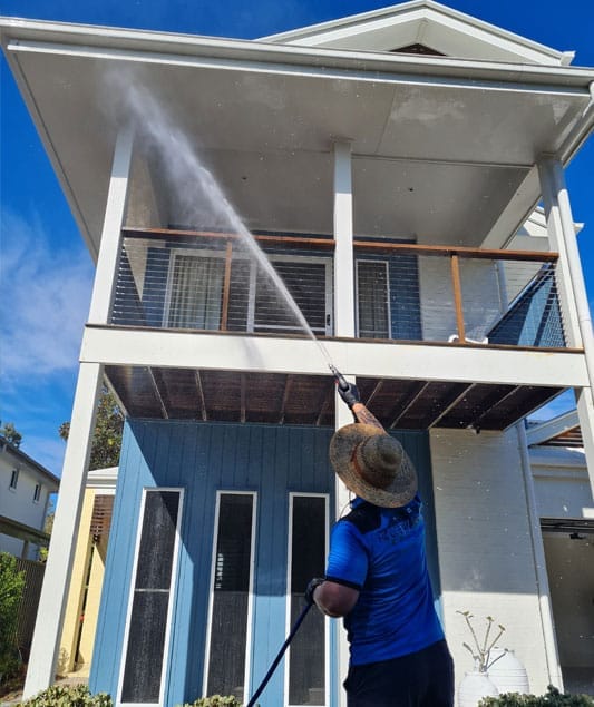 man using high pressure water to clean a house